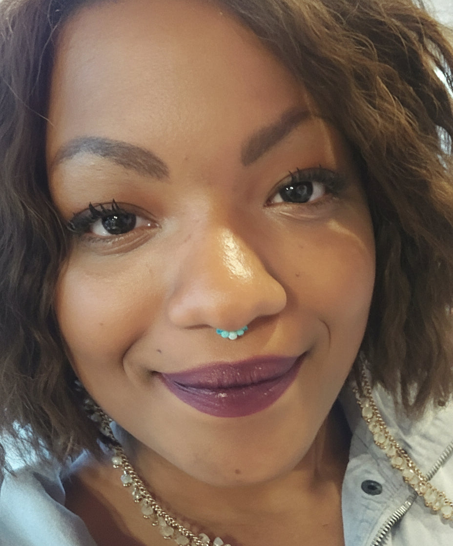 Close-up of a person with a nose ring and layered necklaces.