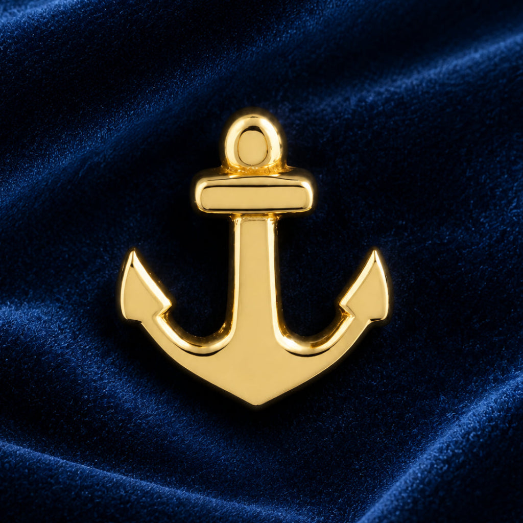 A polished gold anchor-shaped pin or charm displayed on a dark navy blue velvet fabric background.