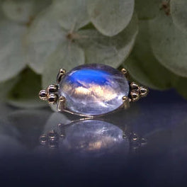 Gold ring with a blue gemstone against a green leafy background