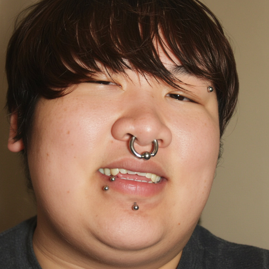 Black and white close-up of a person with multiple piercings including a lip ring and nose ring.
