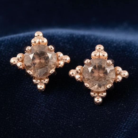 Pair of rose gold earrings with brown gemstones on a dark blue background