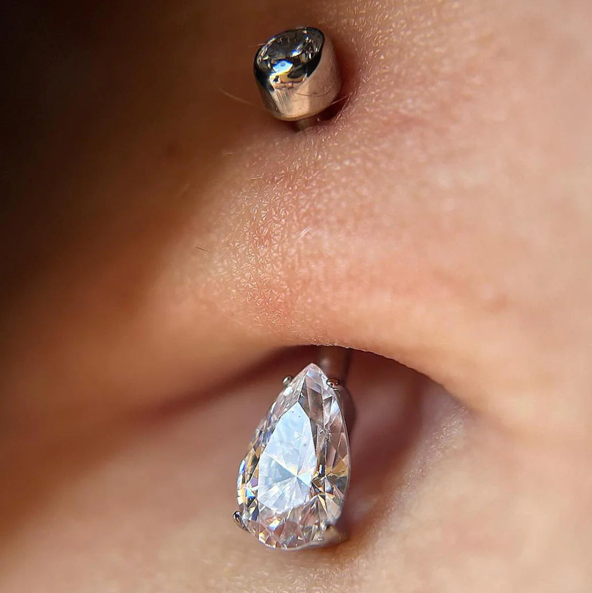 Close-up of a diamond curved barbell on a person's navel with a blurred background
