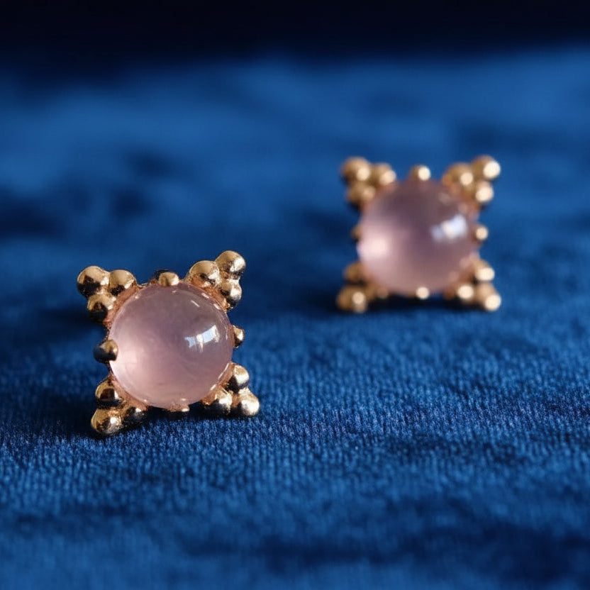 Pair of gold earrings with pink gemstones on a light background