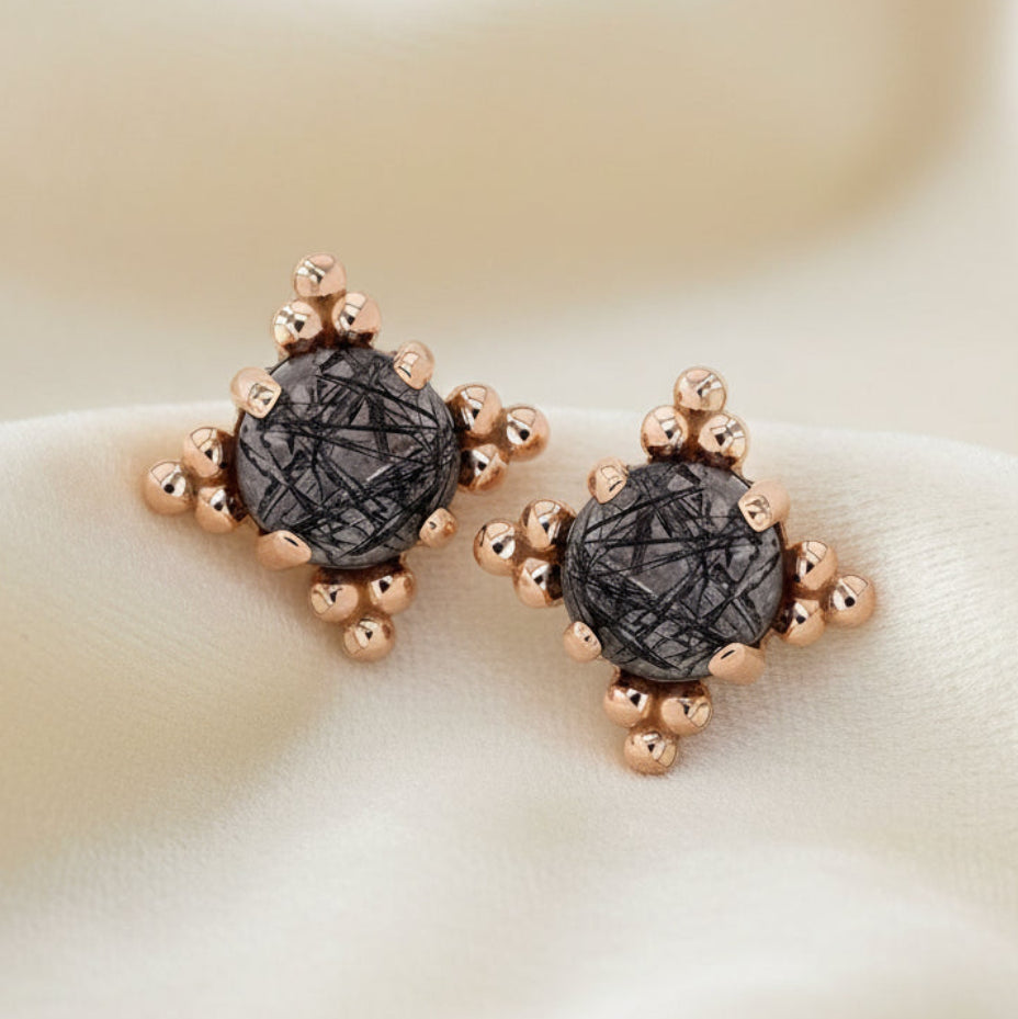 Pair of earrings with rose gold and black stone design on a white background