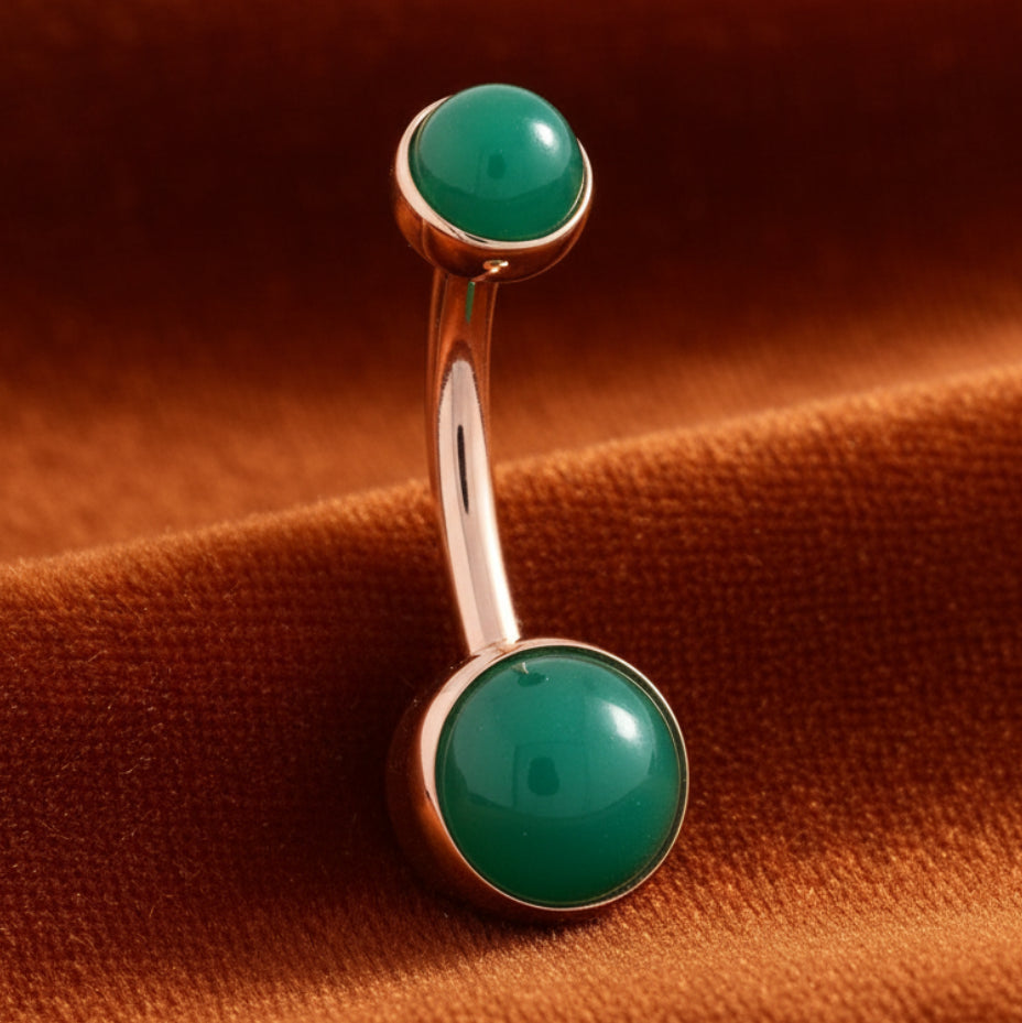 Rose gold belly button ring with green gemstones on a white background