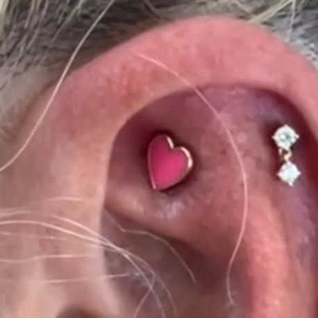 Close-up of an ear with a pink heart-shaped earring and a diamond-studded earring.