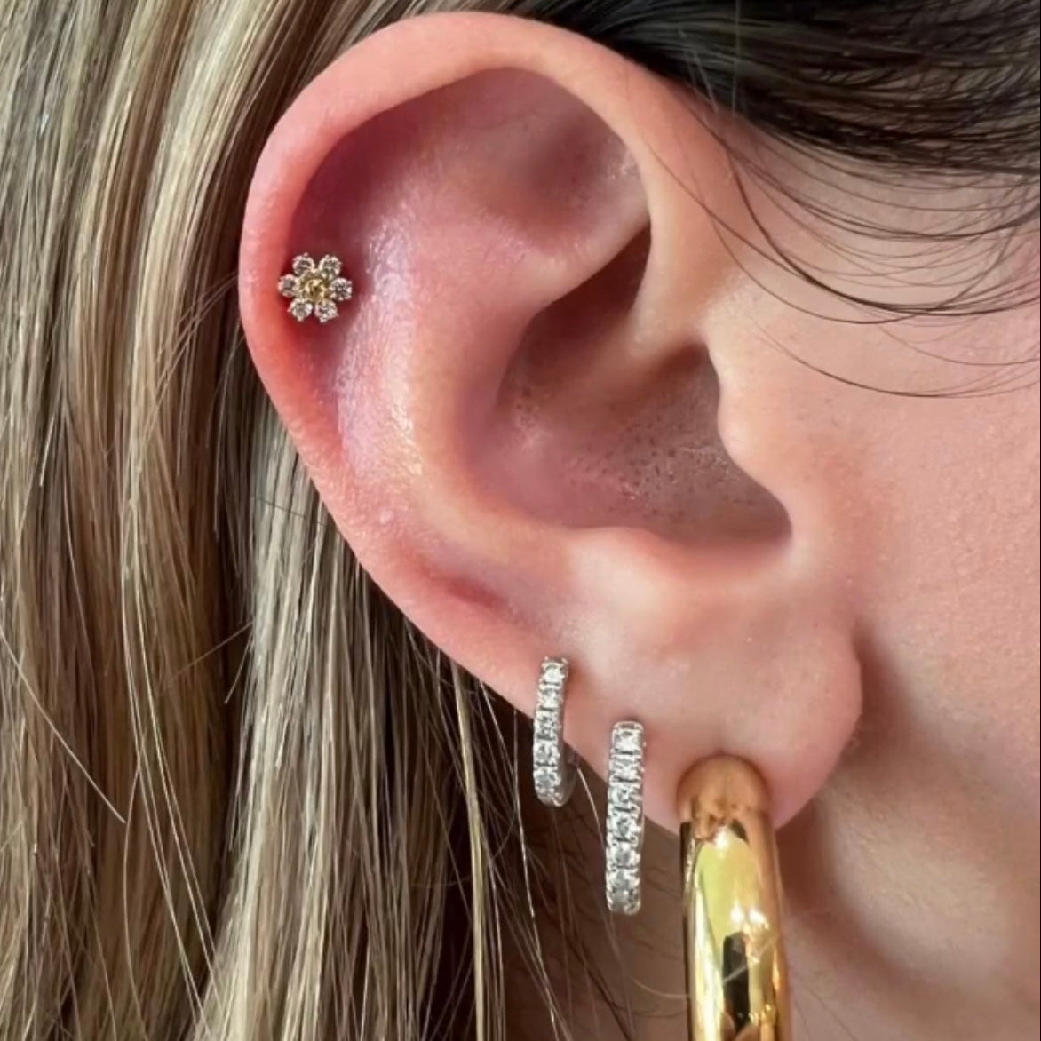 Close-up of an ear with gold hoop earrings and a small floral earring.