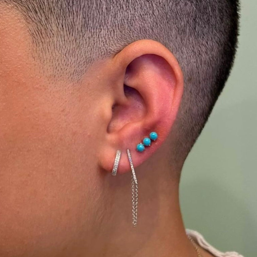 Profile of a person with a shaved head wearing earrings and necklaces.