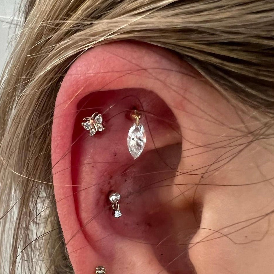 Close-up of an ear with multiple diamond earrings against a neutral background
