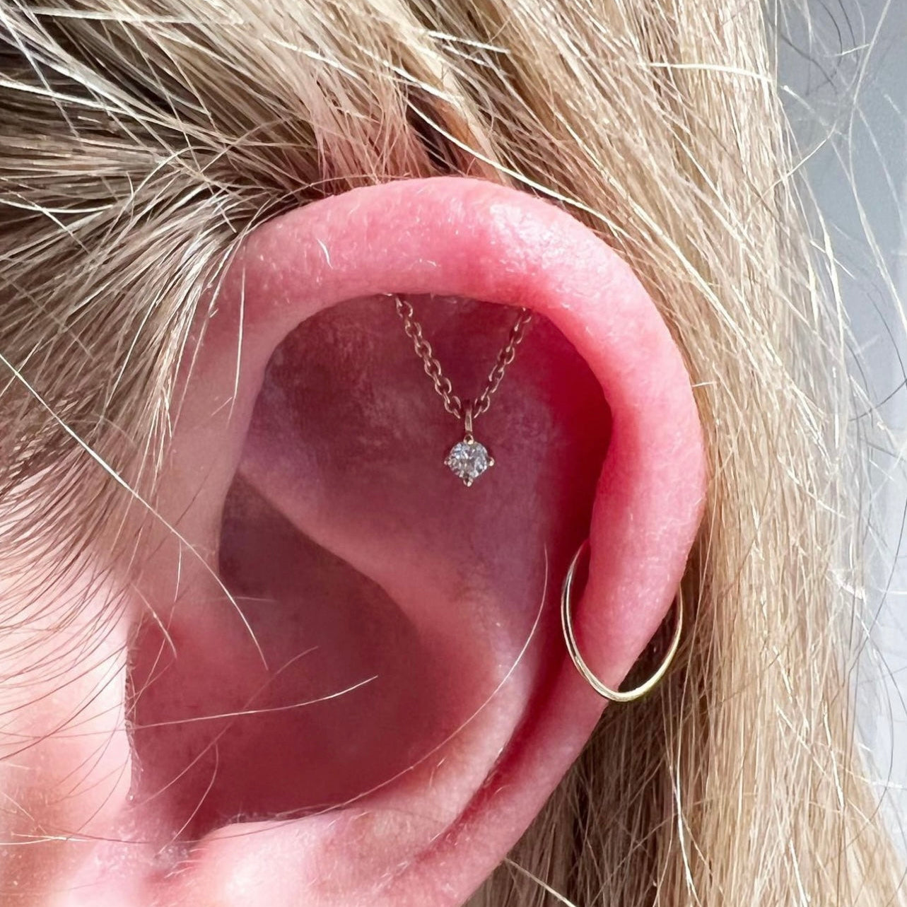Close-up of an ear with a gold hoop earring and a necklace with a diamond pendant.