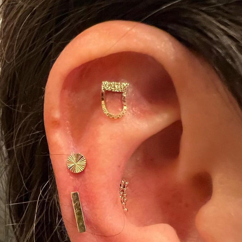 Close-up of an ear with multiple gold earrings and a small red earring.