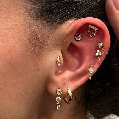 Close-up of a woman's ear with multiple earrings, wearing a gray hoodie.