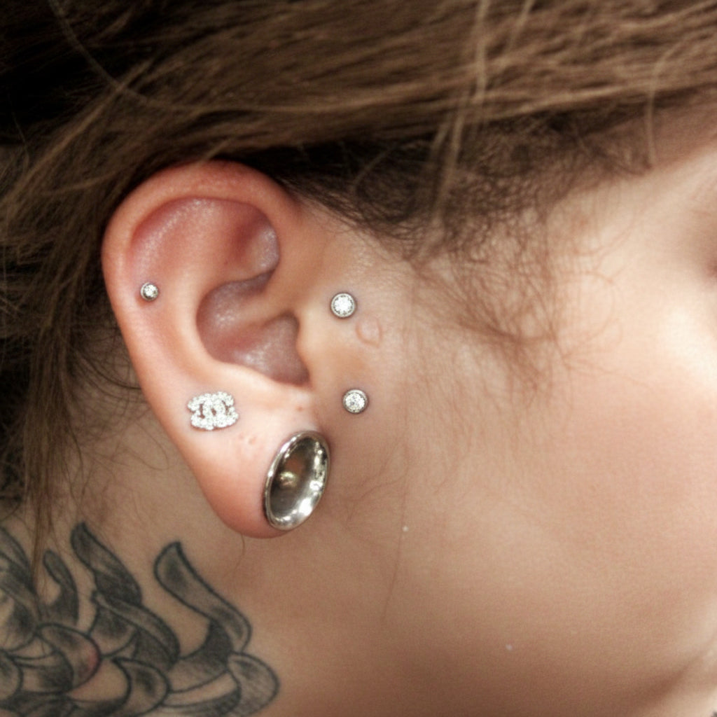Close-up of an ear with multiple piercings and tattoos on the neck.