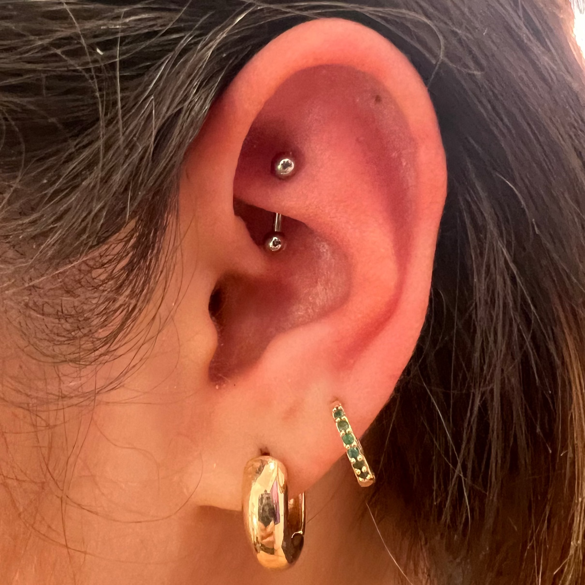 Close-up of an ear with gold hoop earrings and a green gemstone earring.