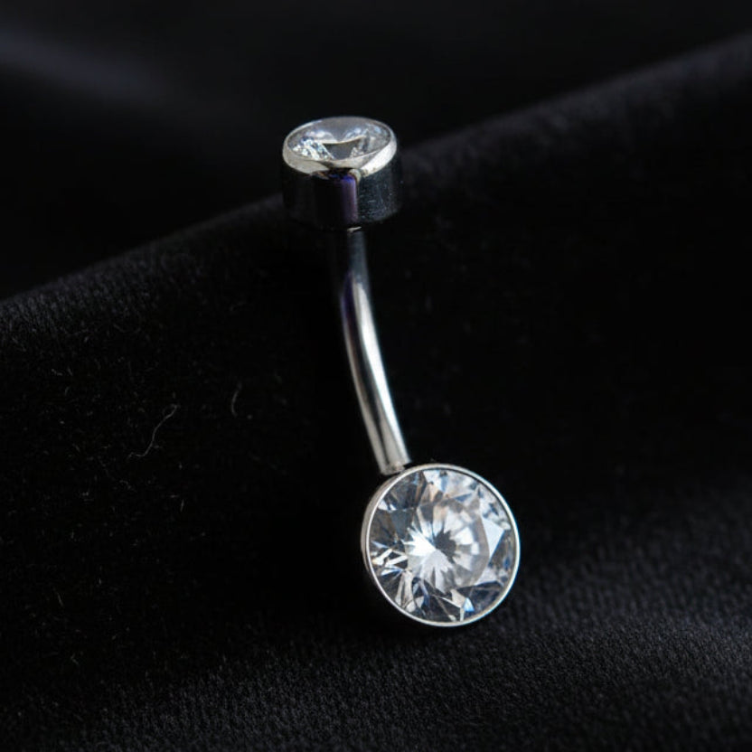 Silver belly button ring with a large gemstone on a textured beige background