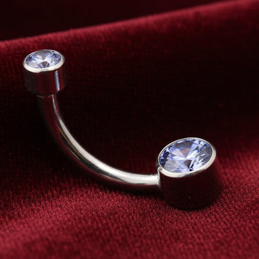 Silver belly button ring with gemstones on a textured beige surface