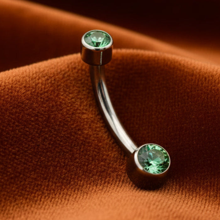 Belly button ring with green gemstone on a stone surface