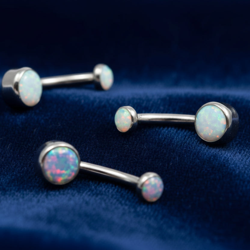 Three silver barbell earrings with opal-colored stones on a white background