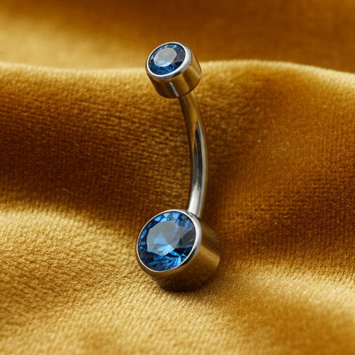Belly button ring with blue gemstones on a mustard yellow fabric background