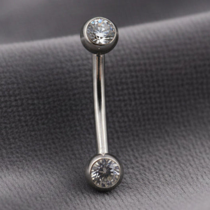 Silver belly button ring with gemstones on a textured white background