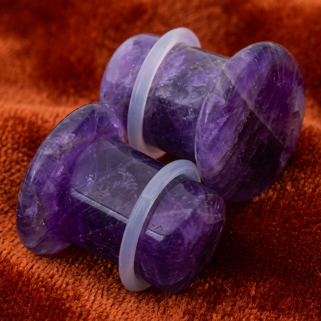 Two purple amethyst ear plugs with translucent white silicone bands, shown on a plain white background.