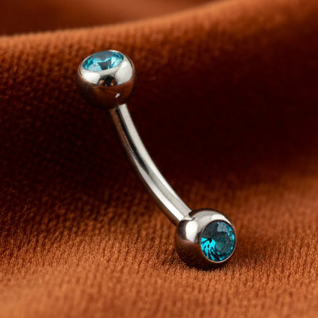 Silver belly button ring with blue gemstones on a white background
