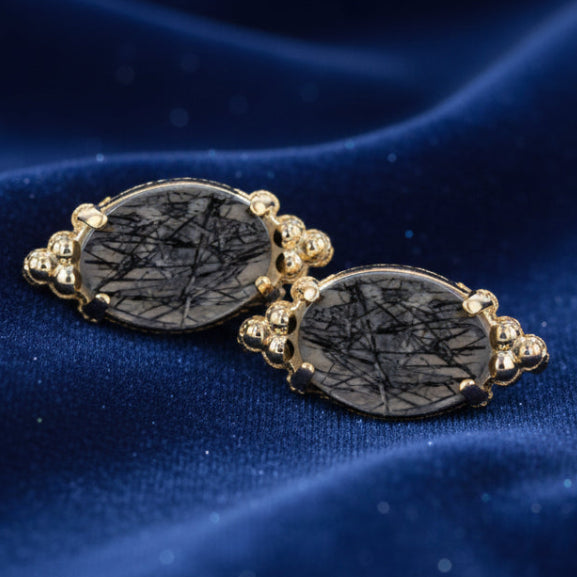 Pair of earrings with black stone and gold accents on a white background