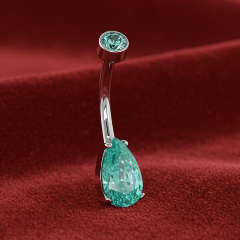 Silver belly button ring with green gemstones on a white background